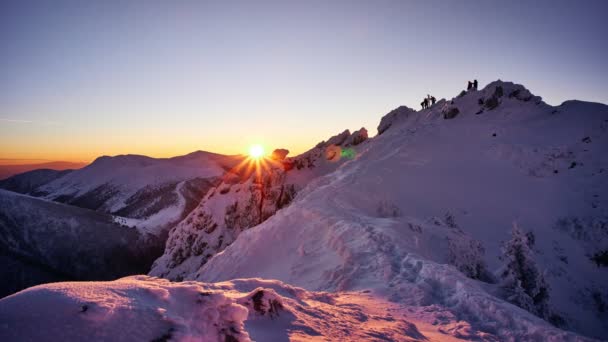 Sonnenuntergang von der Spitze eines verschneiten Berges. Menschen bewegen sich oben auf dem Berg. — Stockvideo