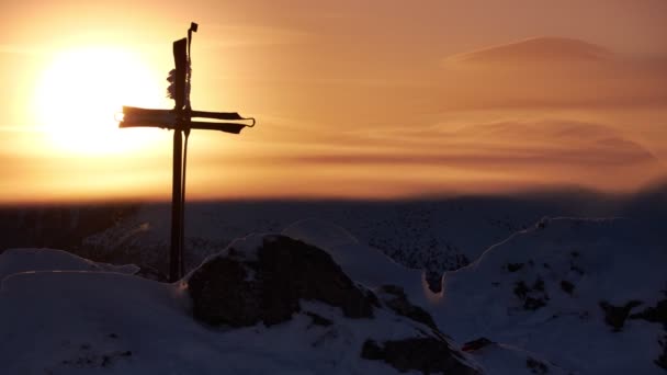 Hierro forjado cruz cristiana en la cima de una montaña durante el invierno. Sol en el cielo naranja, puesta de sol — Vídeos de Stock