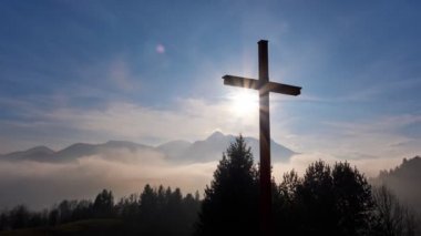 Christian cross in the glow of the sun, mountain landscape above the clouds