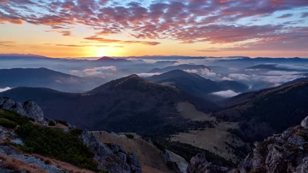Sunrise in a mountain landscape. The clouds are painted in warm colors. Low clouds spill over the hills. — Stockvideo
