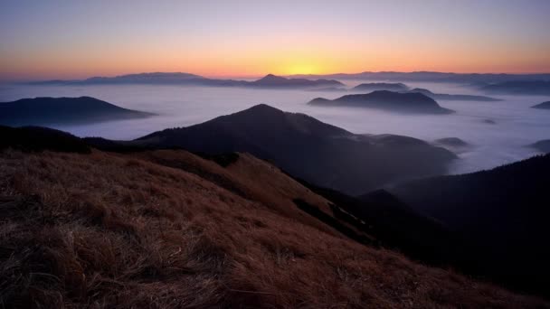 Sunrise in a mountain landscape. Low inverse clouds in the valley between the hills. — Stockvideo