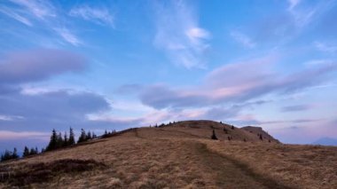 Colorful moving clouds at sunset, grassy ridge of a hill with a hiking trail