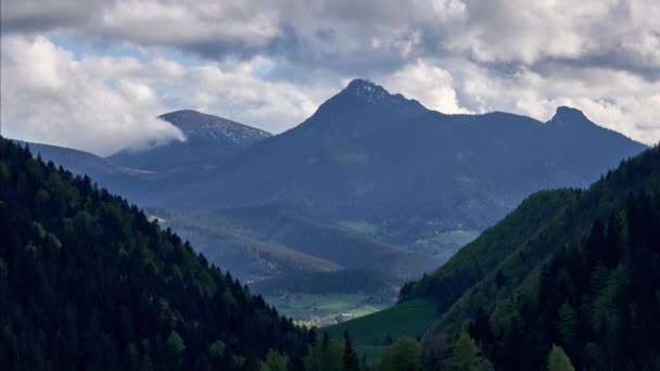 In summer, clouds spill over mountain peaks in a wooded basin — Stock videók