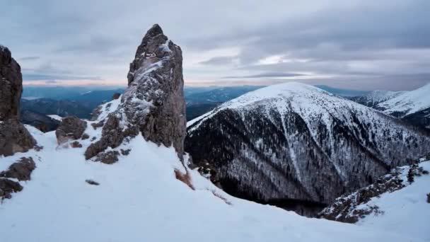 Πυροβολισμός χιονισμένων βουνών. Ένας κοφτερός βράχος προεξέχει από το χιόνι.Στρογγυλός λόφος με έλατα. Σύννεφα — Αρχείο Βίντεο
