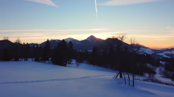 Una vista de un paisaje invernal nevado al atardecer. El sol brilla detrás de las montañas e ilumina el cielo. — Vídeos de Stock