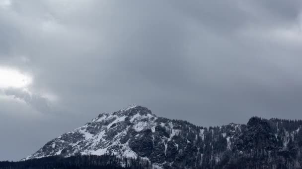 Dichte wolken boven een rotsachtige besneeuwde piek. Winderig winterweer. — Stockvideo