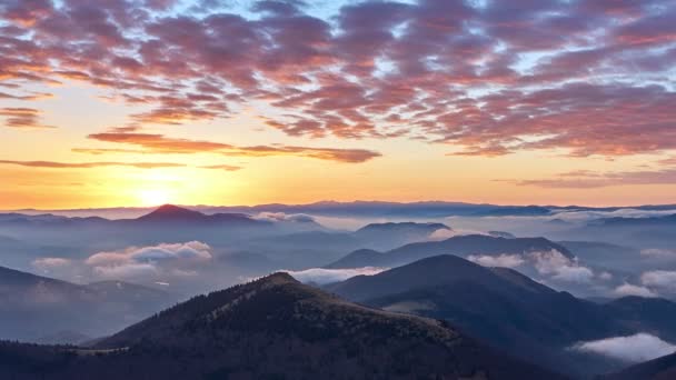 El amanecer en el paisaje montañoso, la niebla se derrama sobre las colinas. Nubes de colores en rojo anaranjado, mañana épica — Vídeos de Stock