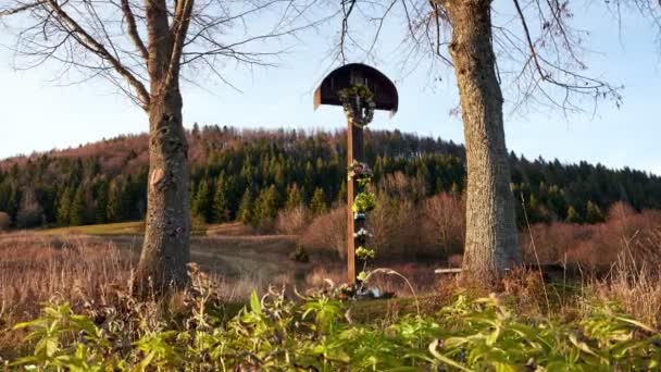 Une vieille croix chrétienne en bois suspendue avec des couronnes et des fleurs. Une place spirituelle parmi les arbres.4K — Video