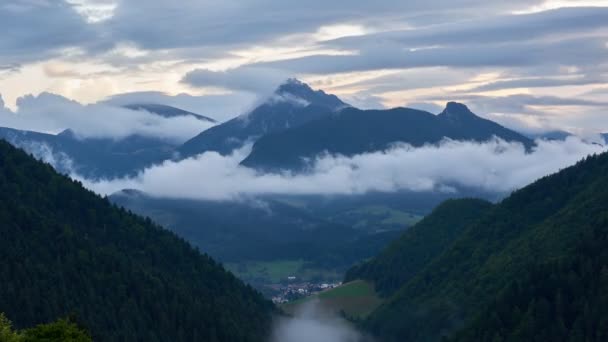 Похмурі гори, заховані в туманних хмарах, є невелике поселення в долині під горами — стокове відео