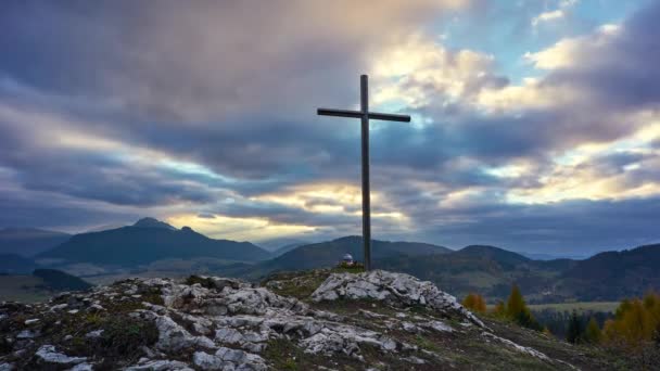 Christelijk kruis op een rots bij zonsondergang, kleurrijke wolken. — Stockvideo