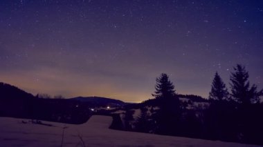 Ormanda kış manzarasında yıldızlı gece gökyüzü. Geceden gündüze geçiş. 4K zaman dilimi