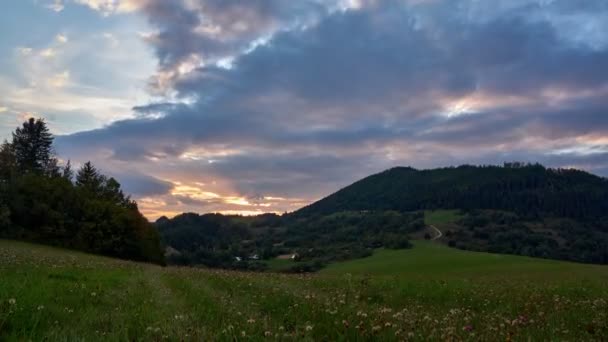 Puesta de sol sobre las colinas en un prado verde en el campo — Vídeo de stock