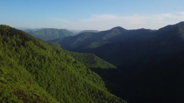 Dikenli, ağaçlık tepeleri olan ağaçlık bir hava manzarası. Bahar ormanı, Karpatlar, Slovakya, tepeleri, ağaçları ve yeşil otlakları olan renkli manzaralar vadi köyünde evler, doğal arka plan 4K