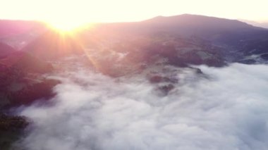 Karpatlar 'da bir dağ manzarasının kırsal kesimindeki sis ve ters bulutların hava aracı görüntüsü, gün doğumunda. Tepelerin ardından Parlak Güneş yükseliyor. FHD drone videosu