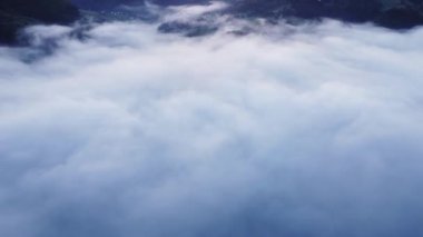 Ağaçların üstündeki dağ ormanı vadisindeki kalın beyaz bulutların havadan görünüşü. Bulut tersine dönüyor. Bulutların tepesi, güneş doğmadan önce sisli manzara.