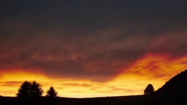 Güneşin batışındaki bir şimşek fırtınasından sonra ağaçlı bir ülkenin siluetinin üzerinde güzel, ateşli bulutlar. Zaman Dilimi 4K