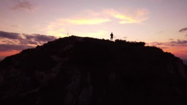Dağ manzaralı destansı bir kayanın üzerinde gün batımına ait drone hava görüntüsüyle duran kişi. Yüksek kalite 4k görüntü