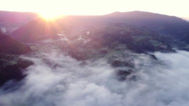 Karpatlar 'da bir dağ manzarasının kırsal kesimindeki sis ve ters bulutların hava aracı görüntüsü, gün doğumunda. Tepelerin arkasından Parlak Güneş yükseliyor. 4K İHA videosu.