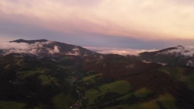 A foothill village in a hilly landscape after the rain at sunset. Formation of new clouds above the hills. Aerial top view