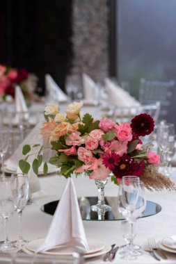 Temiz vazoları ve renkli çiçekleri olan beyaz masa örtüleri. Altın renkli tabaklar, peavh peçeteleri, masa numaraları ve ayna süslemeleri. Düğün günü..