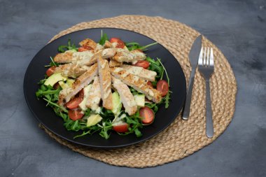 Avokado, roka ve vişneli domatesli tavuk salatası gri taşlı arka planda. Üst görünüm