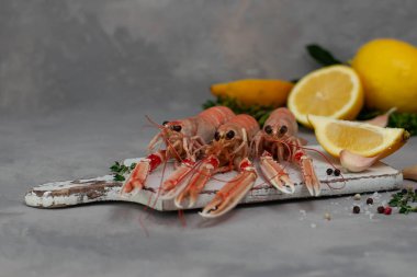Beyaz kesme tahtasında kaynamış Langoustines gri beton masada izole edilmiş. Limon ve baharatlı otlarla servis edilir..