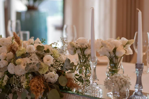 Weiße Tischdecken mit klaren Vasen und weißen Blumen und Farn-Arrangements. Goldfarbene Teller, Peavh Servietten, Tischnummern und Spiegelmittelstücke. — Stockfoto