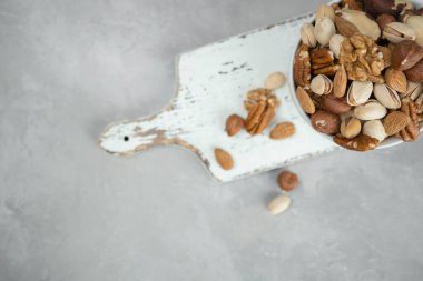 Badem, şam fıstığı ve kaju, açık gri bir zemin üzerinde keten peçetenin üzerindeki ahşap bir kaseye konur. Üst görünüm ve kopyalama alanı.