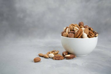 Badem, şam fıstığı ve kaju, açık gri bir zemin üzerinde keten peçetenin üzerindeki ahşap bir kaseye konur. Üst görünüm ve kopyalama alanı.