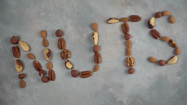 Слово орехи из смеси орехов на светло-сером фоне. — стоковое видео