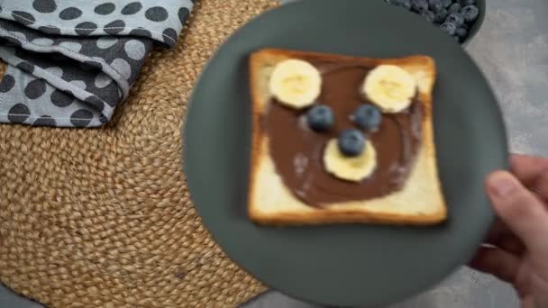 Barn frukost eller lunch eller mellanmål toast med choklad hasselnöt spridning, banan och blåbär formade som söt björn. — Stockvideo