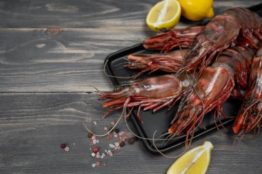Siyah tabakta çiğ kaplan karidesi ve limon dilimleriyle süslenmiş ahşap masa. Taze deniz ürünleri..