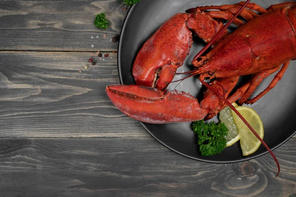 Istakoz, ahşap masadaki siyah tabakta limon dilimleriyle süslenmiş. Taze deniz ürünleri. Lüks yemekler..