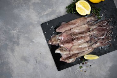 Siyah taş tabakta çiğ deniz mürekkep balığı pişmeye hazır. Üst Manzara. Karanlık bir arka planda. Taze deniz ürünleri..