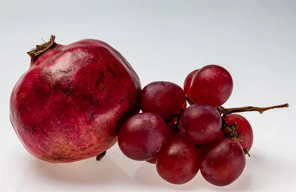 Kırmızı nar ve hafif arkaplanda üzüm demetleri. Hayat meyvesi geçmişi.