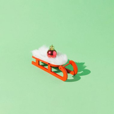 Üzerinde Noel süsü olan kırmızı ve beyaz bir kızak. Asgari yaratıcı fikir. Kış arka planı, yeşil. 2022