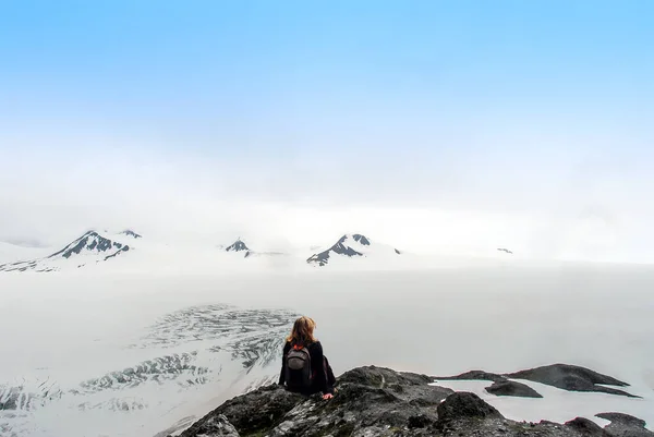 女徒步旅行者坐在山顶上俯瞰阿拉斯加的哈定冰原 欣赏纳塔克山和覆盖着雪的高山的美景和超现实美景 — 图库照片