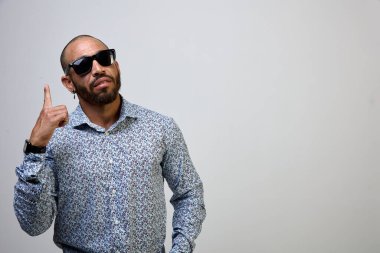 Sakallı, tişörtlü, havalı, kendine güveni tam bir Latin adam, parmağını kaldırmış, beyaz arka planda soyutlanmış.