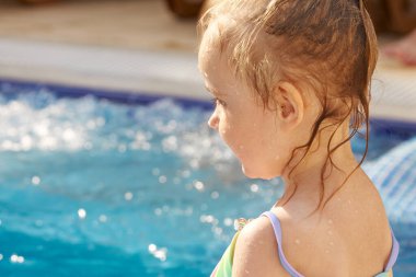 Gökkuşağı mayo giymiş, bilardo oynayan ve güneşin altında gülümseyen küçük tatlı bir kız.