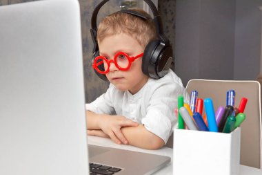 Kırmızı gözlük ve kulaklık takan bir çocuk dizüstü bilgisayarından içeriği izliyor.