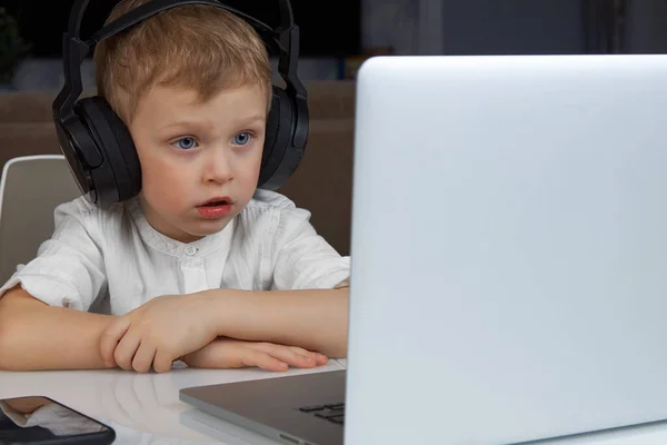 Αγόρι που φοράει ασύρματα ακουστικά, κάθεται σε ένα γραφείο, χρησιμοποιώντας ένα φορητό υπολογιστή — Φωτογραφία Αρχείου
