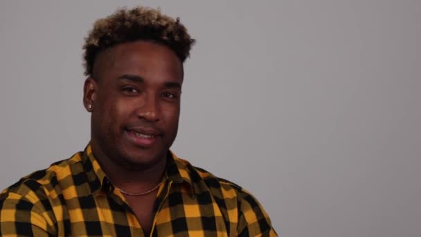 Junger Afroamerikaner trägt kariertes Hemd, blickt in die Kamera und lächelt. — Stockvideo