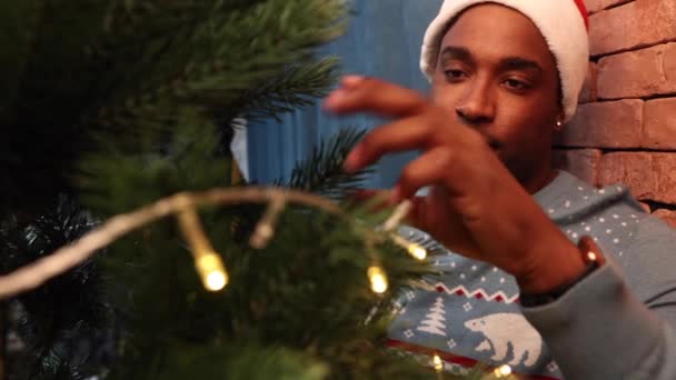 Africano homem americano em suéter e um chapéu decora a árvore de Natal — Vídeo de Stock