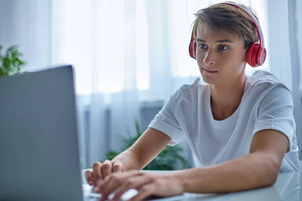 Έφηβος με ακουστικά εργάζεται ή διδάσκει στο σπίτι στο laptop του . — Φωτογραφία Αρχείου