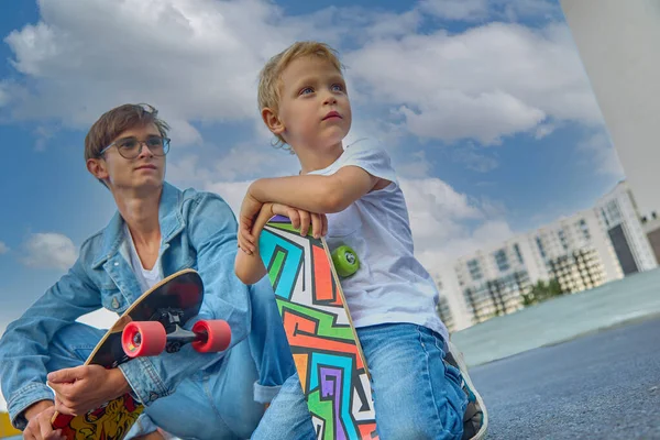 Rapaz feliz e seu irmão mais velho montam o skate no exterior. — Fotografia de Stock