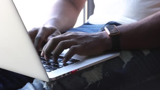 Czarny mężczyzna pisze na klawiaturze laptopa siedząc na parapecie — Wideo stockowe