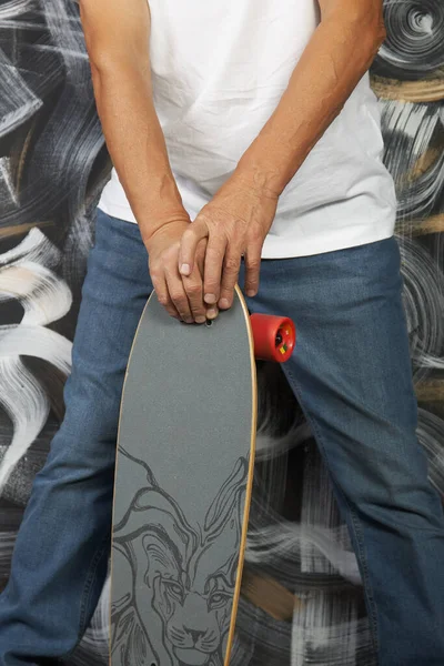 彼の手の中にスケートボードとジーンズやスニーカーでファッショナブルな男の足をクローズアップ. — ストック写真