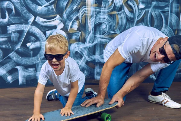 Прохолодний спортивний дід показує скейтборд з здивованим онуком в сонцезахисних окулярах . — стокове фото