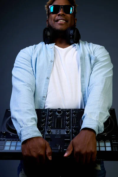 Sonriente DJ afroamericano con un peinado afro sostiene equipo de música. — Foto de Stock