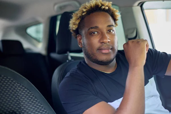 Un hombre afro-americano confiado y serio con una camiseta está sentado en su auto.. — Foto de Stock